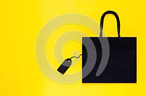 Black shopping paper bag with blank black price tag on yellow background