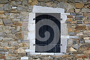 Black shuttered window in stone wall of building