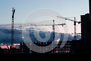 Black silhouette of a construction crane, dramatic sky. Residential building construction, night photography