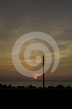 Black silhouette of a lamppost on the sea promenade with tetrapods against the background of the ocean under the evening sunset