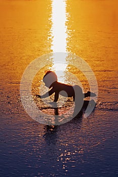 Black silhouette of little child on wet sunset beach