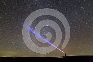 Black silhouette of man with head flashlight on grassy field under beautiful dark summer starry sky.