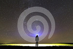 Black silhouette of man with head flashlight on grassy field under beautiful dark summer starry sky.