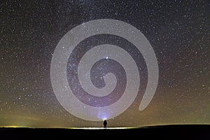 Black silhouette of man with head flashlight on grassy field under beautiful dark summer starry sky.