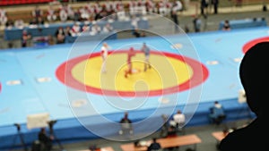 Black silhouette of man`s head in back light. Fan watches duelling on sambo. View of duelling is unfocused.