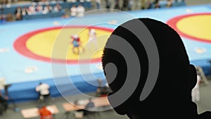 Black silhouette of man`s head in back light. Fan watches duelling on sambo. View of duelling is unfocused.