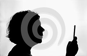 Black silhouette in profile, of woman consulting her smartphone, on white background, horizontally