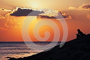 Black silhouette of thinking man sitting alone on sea beach