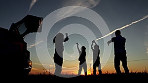 Black silhouettes of family bounce near car at sunset