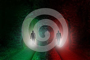 Black silhouettes of two people walking along two different railway tracks into a red and green tunnel, concept of manâ€™s choice