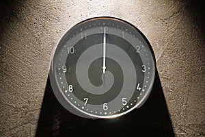 Black simple analog clock in the centre close up showing midnight hanging on the wall with shadows