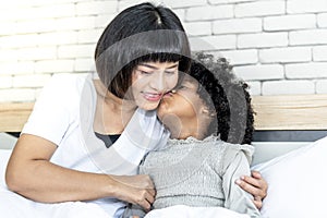 black skin African girl kissing her mother`s cheek with love on white bed