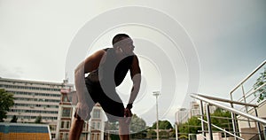 A Black-skinned athlete in a black sports summer uniform finishes his run, exhales and descends into the room under the