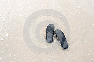 Black slippers on the beach touched by waves from the sea