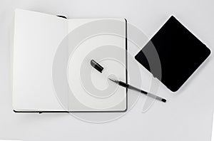 Black small closed square notepad and large open notebook with blank white pages and ballpoint pen with cap on white back