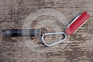 A black small flashlight and a red folding knife on a gray iron carabiner latch