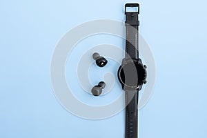 black smart watch and wireless headphones on blue background. Blank screen. copy space