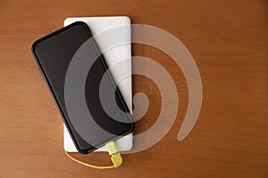 Black smartphone being charged by a white power bank on top of a wooden table.