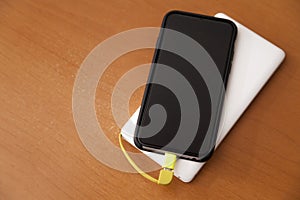 Black smartphone being charged by a white power bank on top of a wooden table.