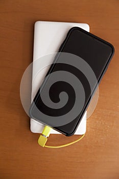 Black smartphone being charged by a white power bank on top of a wooden table.