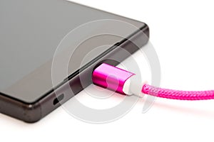 Black smartphone charging. Pink micro usb cable pluged in mobile phone. Isolated on white