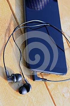 Black smartphone and headphones on a wooden light brown background