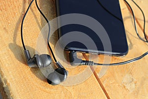 Black smartphone and headphones on a wooden light brown background