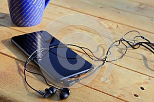 Black smartphone and headphones on a wooden light brown background