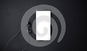 Black smartphone and headset on black background. Top view with copy space photo