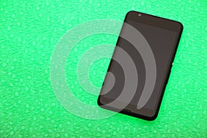 Black smartphone lies on a bright green background. The background is highlighted below