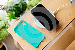 Black smartphone and mint silicone case is charged from a wireless charger.