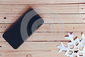 black smartphone with white snowflake on a wooden table background with snow sparkle