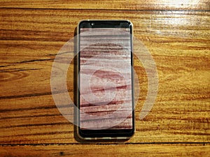 Black smartphone on wooden background with smartphone screen replicating the same wooden texture