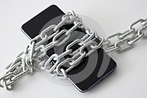 Black smartphone wrapped in metal chain closeup