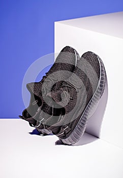 Black sneakers on blue background with white podium in form of geometric cube.