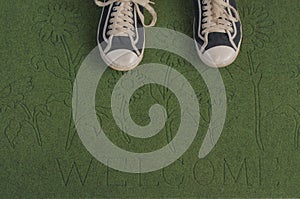 Black sneakers on a green welcome mat