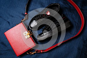 Black sneakers with red tongues and a red bag with a golden lock on a blue woven background