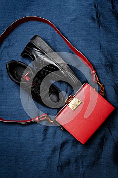 Black sneakers with red tongues and a red bag with a golden lock on a blue woven background