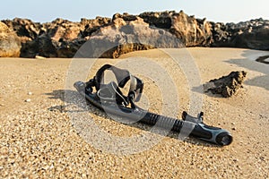 Black snorkel and diving mass on beach sand, small rocks in background. Shot through wet lens drops make parts of picture blurry