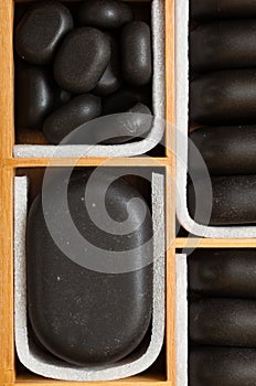Black spa zen massage stones in wooden case as background