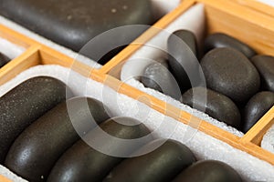 Black spa zen massage stones in wooden case as background