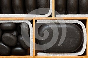 Black spa zen massage stones in wooden case as background