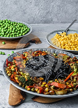 Black spaghetti or pasta from seafood with grilled vegetables, broccoli, corn, green peas in plate on light gray backgroud.