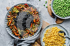 Black spaghetti or pasta from seafood with grilled vegetables, broccoli, corn, green peas in plate on light gray backgroud.