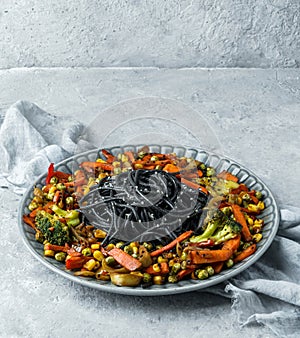 Black spaghetti or pasta from seafood with grilled vegetables, broccoli, corn, green peas in plate on light gray background.