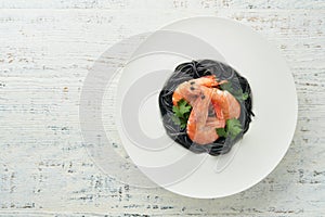 Black spaghetti pasta shrimp on black plate on wooden white table background. Squid ink pasta with prawns. Pasta seafood. Top view