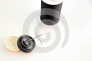 Black spool of thread, needle, and black and white buttons