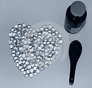 A black spoon, dark bottle and Omega-3 lying in the shape of a heart on white background.