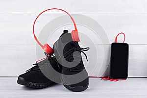 On black sport shoes are wearing red headphones for music next to a mobile phone on a light background
