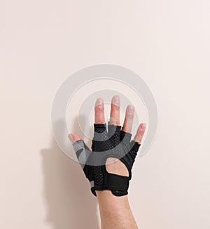 Black sports glove on a female hand, beige background. Part of the body is lifted up